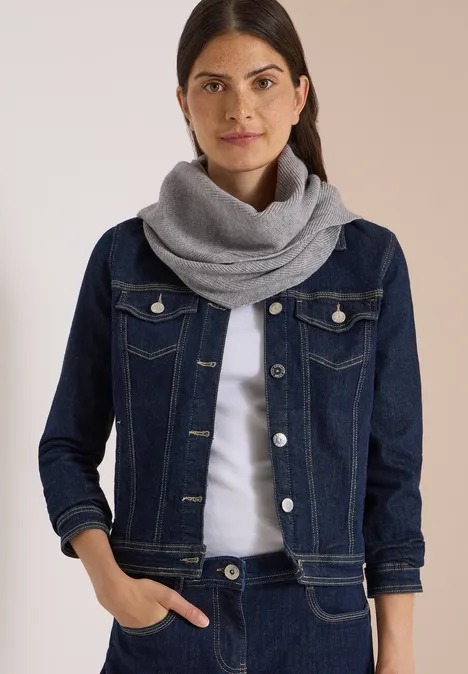 Femme aux cheveux foncés portant une veste en jean bleue et une écharpe grise.