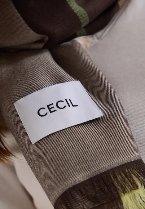 Gros plan d'un vêtement beige avec une étiquette blanche portant l'inscription noire CECIL.