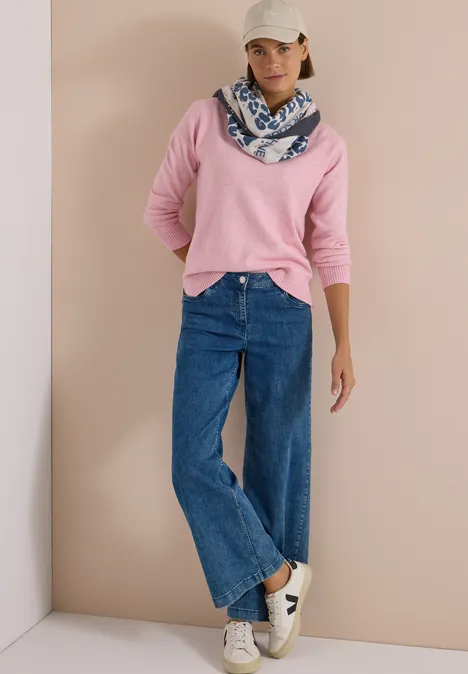 Foulard triangulaire à motif léopard dark navy blue Frau in rosa Pullover, weite blaue Jeans, weißer Cap, gemusterter Schal und weißen Sneakern vor schlichtem Hintergrund.