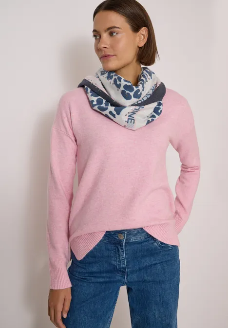 Foulard triangulaire à motif léopard dark navy blue Frau trägt rosafarbenen Pullover, blaue Jeans und gemusterten Schal vor neutralem Hintergrund.