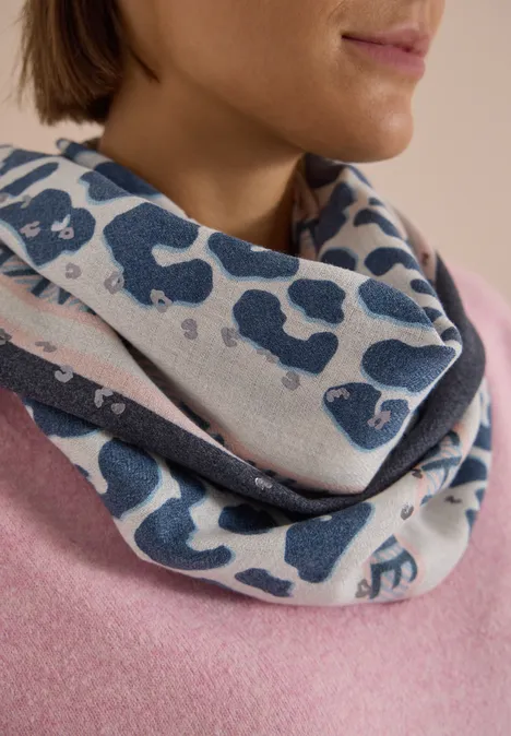 Foulard triangulaire à motif léopard dark navy blue Eine Frau trägt einen lässigen Loop-Schal mit blauem Leopardenmuster über einem rosa Pullover.