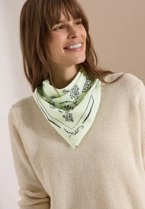 Persoon in beige trui draagt een lichtgroen sjaaltje met zwarte bloemenprint.