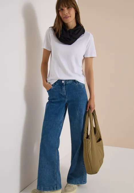 Écharpe Loop unie Black Femme en T-shirt blanc, jean évasé, foulard noir et sac vert devant un mur beige.