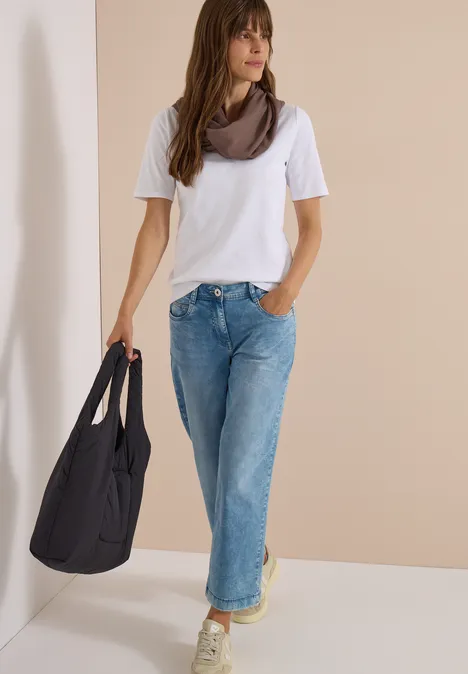 Écharpe Loop unie urban taupe Femme en t-shirt blanc, jean ample et foulard, tenant un grand sac noir, posant devant un mur beige.