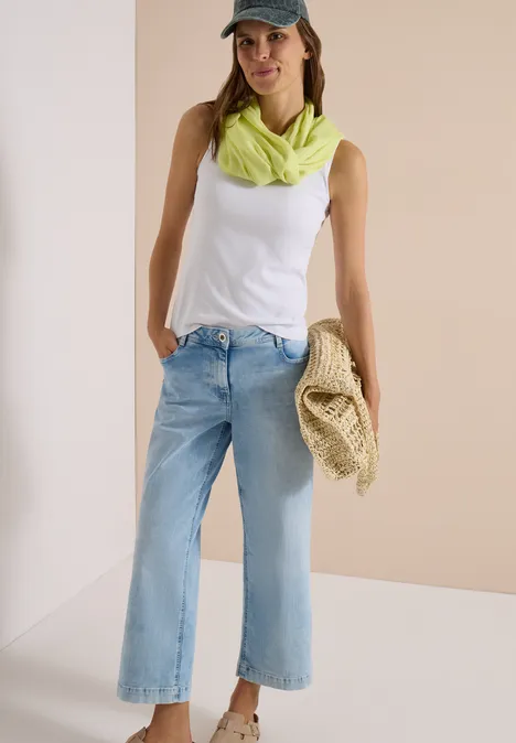 Écharpe Loop unie citrin green Femme en débardeur blanc, jean clair large, foulard vert néon et casquette, tient un sac en paille.
