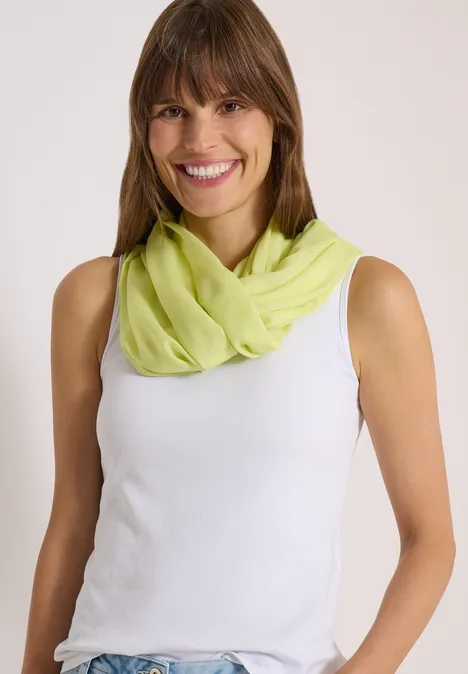 Écharpe Loop unie citrin green Femme souriante aux cheveux bruns, haut blanc sans manches et écharpe vert clair.