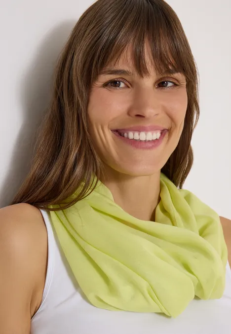 Écharpe Loop unie citrin green Une femme souriante en débardeur blanc porte un foulard vert clair devant un fond neutre.