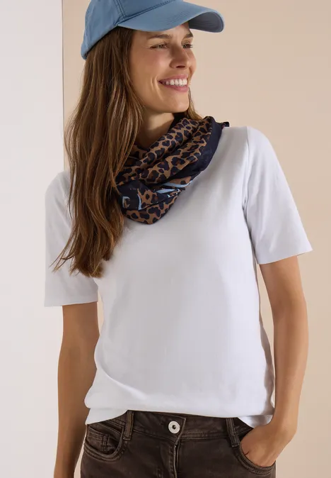 Écharpe Loop à motif léopard creamy mocha Femme souriante avec casquette bleue, t-shirt blanc et foulard imprimé, main dans la poche.