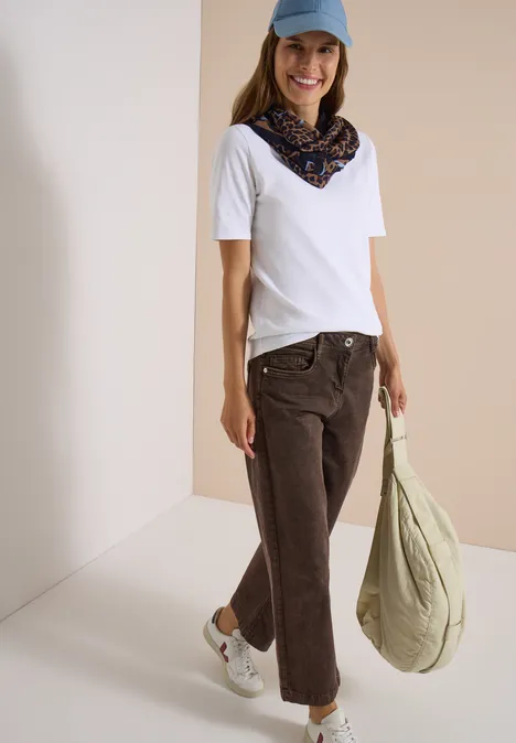 Écharpe Loop à motif léopard creamy mocha Femme en t-shirt blanc, jean marron, casquette bleue et foulard, avec sac vert, souriante.