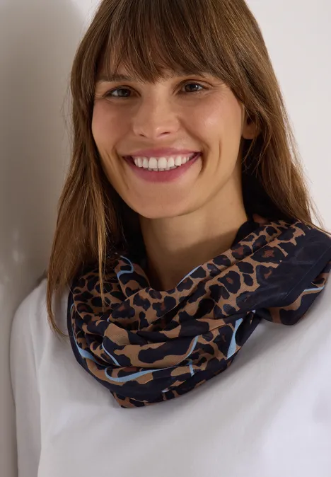 Écharpe Loop à motif léopard creamy mocha Portrait d'une femme souriante aux cheveux bruns, portant un haut blanc et une écharpe infinie léopard bleu et marron.