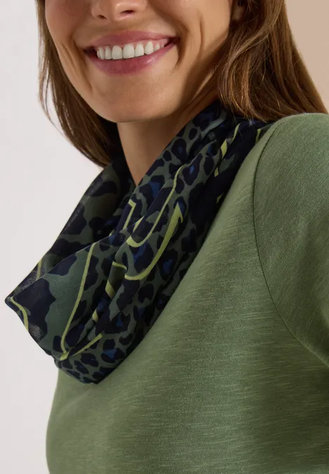 Écharpe Loop à motif léopard dried olive green Femme souriante en haut vert et tour de cou vert foncé à motif léopard.