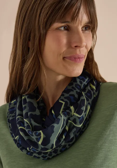 Écharpe Loop à motif léopard dried olive green Gros plan d’une femme aux cheveux bruns portant une écharpe bleu nuit à motif vert.