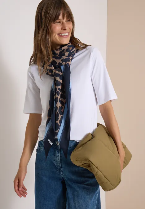 Vrouw in wit t-shirt met blauw sjaal en groen kussen in haar hand.