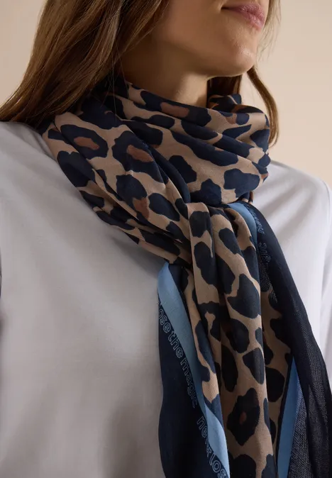 Vrouw in wit shirt draagt een beige-blauwe leopardprint sjaal om haar hals geknoopt.