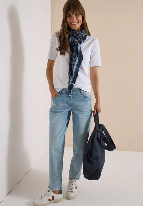 Vrouw in wit T-shirt, lichte jeans, geruite sjaal en blauwe tas.