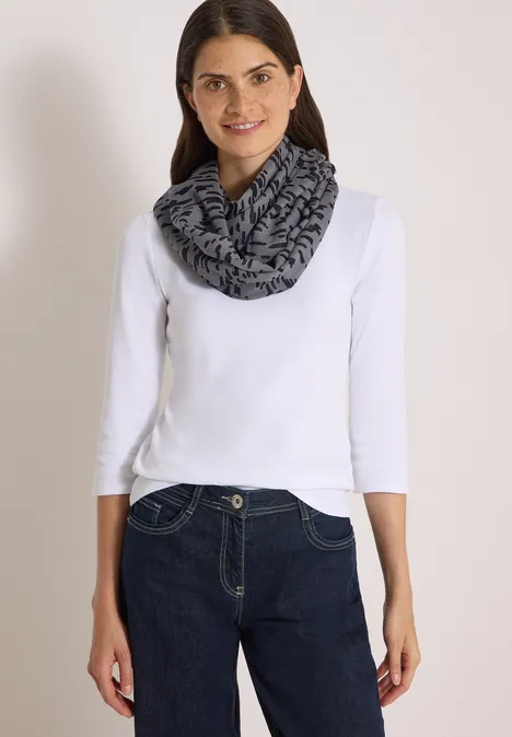 Femme en t-shirt à manches longues blanc, jean foncé et écharpe tube grise et noire.