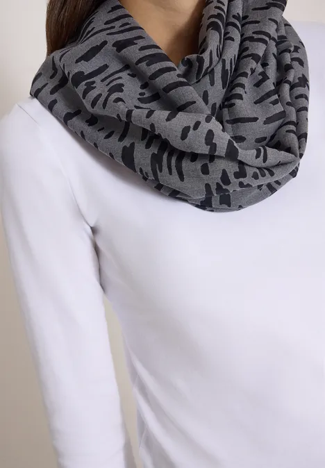 Écharpe grise à motif camouflage noir, drapée sur un haut blanc.