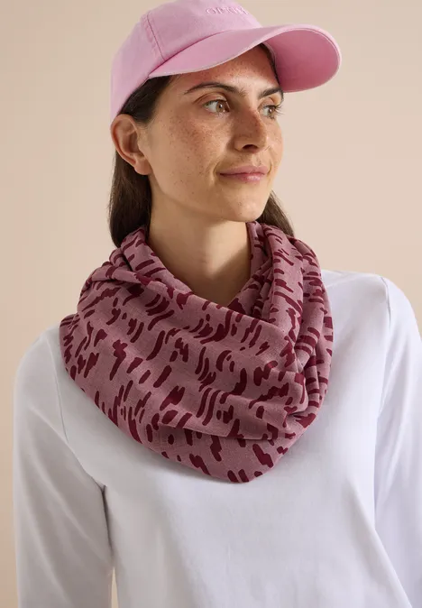 Femme portant une casquette rose et un tour de cou à motifs, t-shirt blanc, fond neutre.