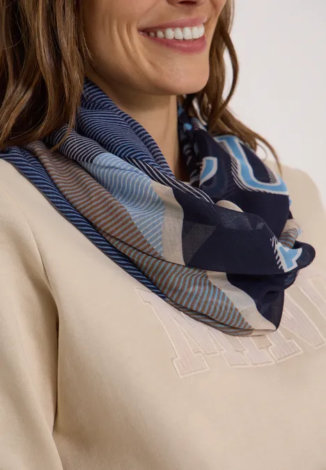 Femme avec foulard bleu à motifs autour du cou, pull beige et sourire discret.