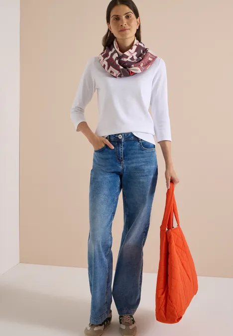 Femme en t-shirt blanc 3/4, jean ample et foulard imprimé, tenant un sac orange.