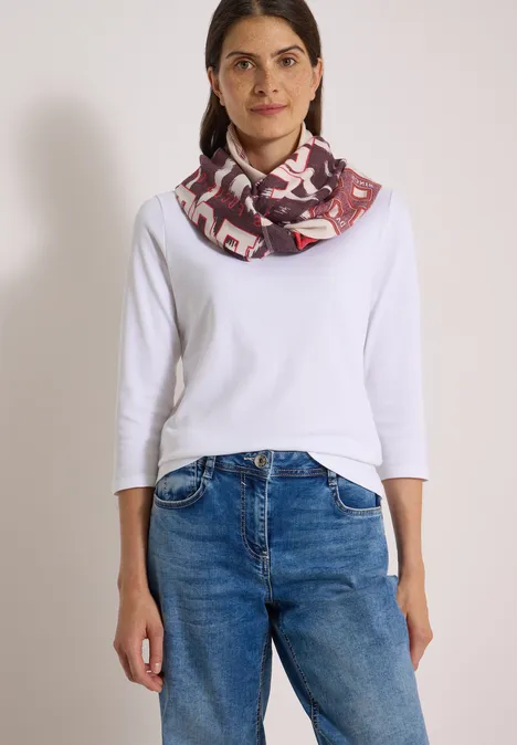 Femme portant un t-shirt blanc à manches longues, un jean bleu et un foulard tube à motifs.