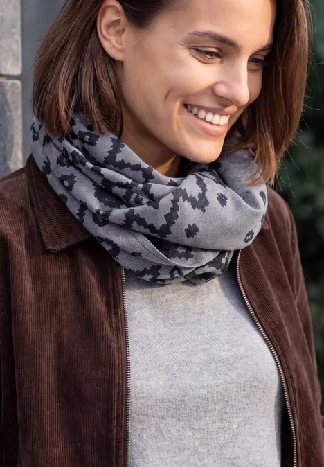 Eine lächelnde Frau mit einem grauschwarzen Schal, brauner Jacke und grauem Pullover.