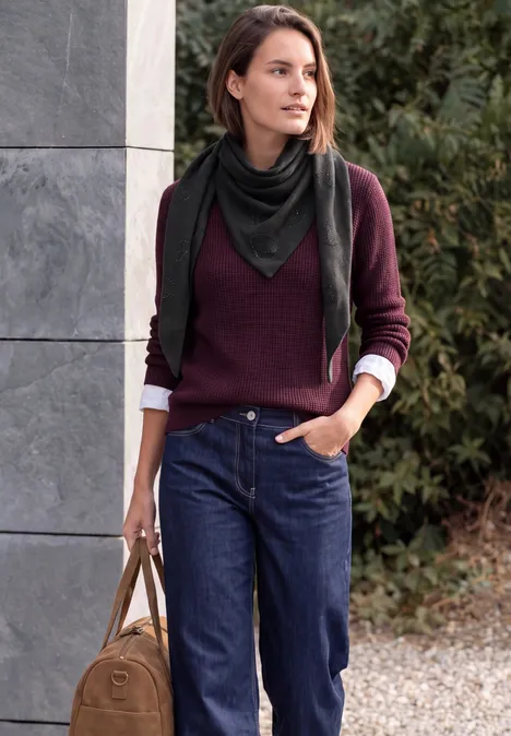 Dreieckstuch mit Glitzerdetails Black Frau in Jeans, weinrotem Pullover und schwarzem Schal trägt Tasche und lehnt an Wand.