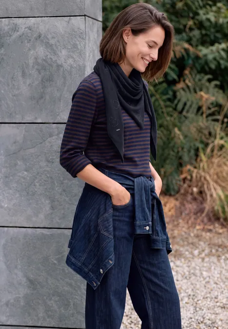 Dreieckstuch mit Glitzerdetails urban dark blue Frau lehnt lächelnd an grauer Wand, trägt gestreiftes Shirt, Jeanshose und hat eine Jeansjacke um die Hüften gebunden.