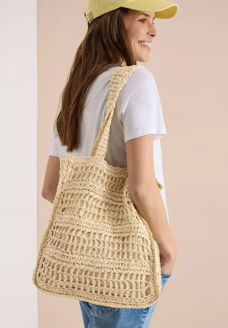 Frau von hinten trägt weißes T-Shirt und eine gehäkelte Strohtasche über der Schulter.