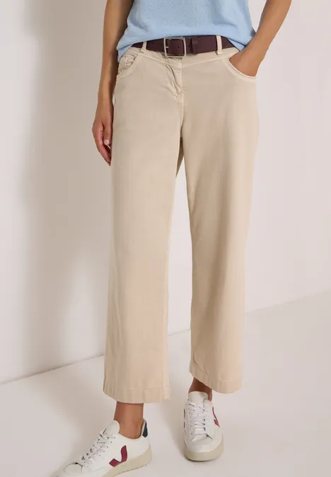 Basic riem met vierkante gesp Raisin Frau trägt beige, weite Hose mit geradem Bein und weiße Sneaker vor heller Wand.