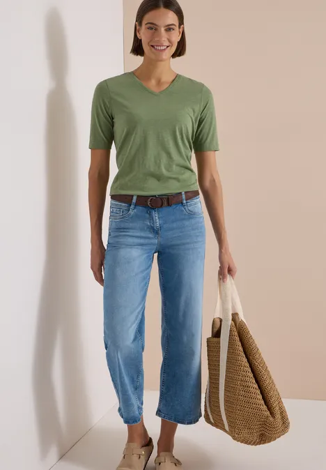 Gürtel mit Streifenmuster Suede Brown Frau im grünen V-Shirt, hellblauen Jeans, braunem Gürtel und großer Korbtasche.