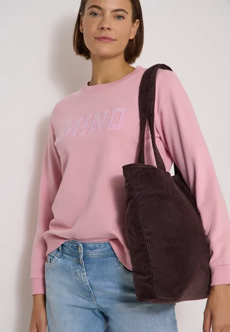 Femme en pull rose DKNY, jean bleu clair et grand sac épaule brun foncé.