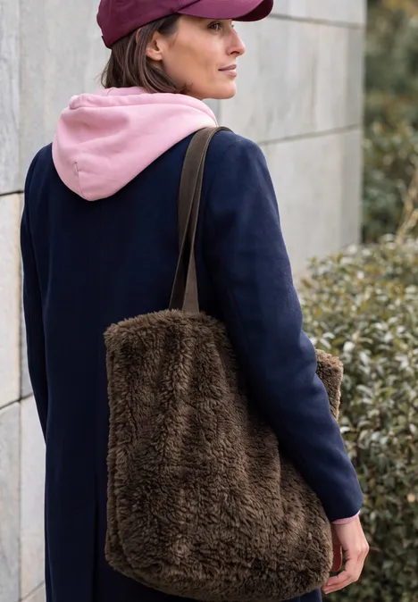 Shopper chocolate sauce brown Frau von hinten trägt marineblauen Mantel, rosa Kapuzenpullover und eine große braune, flauschige Tasche.