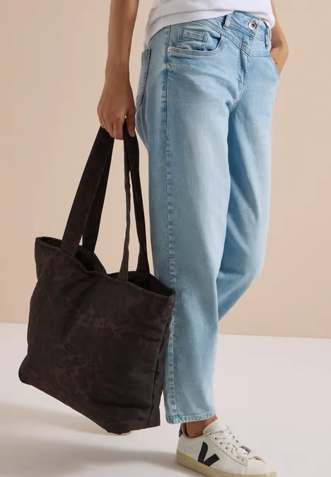 Vrouw in blauwe jeans en witte sneakers draagt een grote zwarte handtas.
