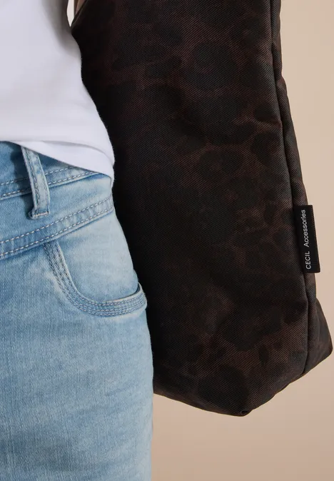 Close-up van persoon in jeans met een bruine tas met logo tegen neutrale achtergrond