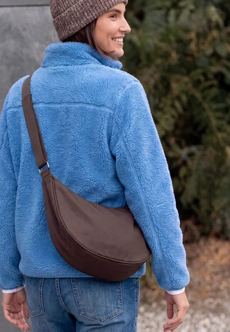 Umhängetasche berry red Frau von hinten in blauer Fleecejacke, Jeans, brauner Umhängetasche und Beanie im Outdoor-Umfeld.