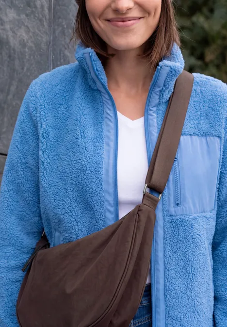Umhängetasche berry red Frau in hellblauer Fleecejacke mit weißem Shirt und brauner Umhängetasche.