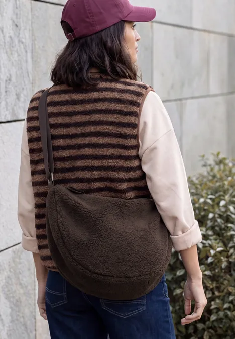 Umhängetasche chocolate sauce brown Frau von hinten mit gestreiftem Strickpullunder, Jeans, roter Kappe und großer brauner Teddy-Fleece-Tasche.