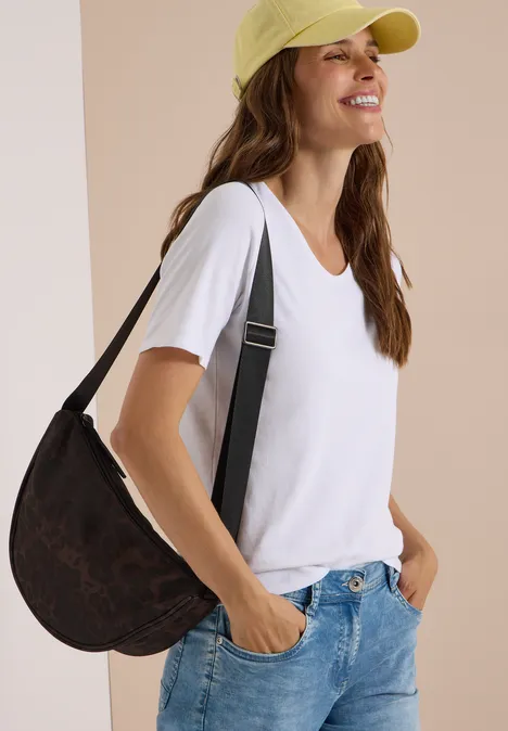 Junge Frau in weißem T-Shirt und Jeans, mit gelber Kappe und Schultertasche, lächelnd seitlich blickend.