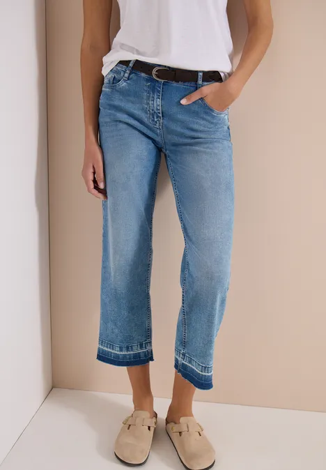 Person trägt hellblaue gerade geschnittene Jeans und beige Loafer vor neutralem Hintergrund.