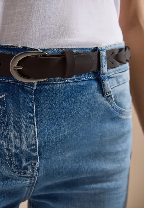 Nahaufnahme einer Person in Jeans mit geflochtenem braunen Gürtel und weißem Oberteil.