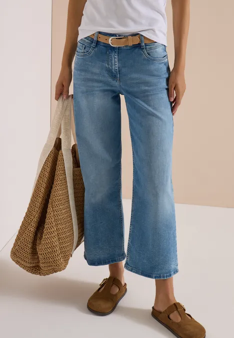Persoon draagt wit shirt, wijde lichtblauwe jeans, bruine schoenen en draagt een strooien tas.