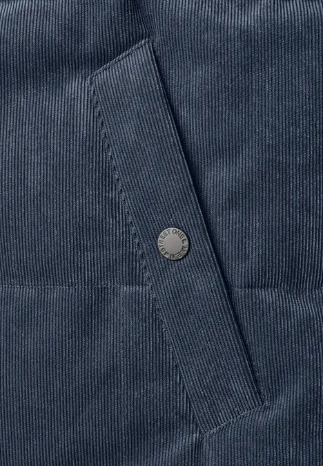 Nahaufnahme eines dunkelblauen Cordstoffs mit Taschenklappe und Metall-Druckknopf.