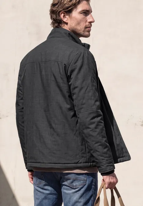 Veste à col montant et fermeture zip ash grey melange Ein Mann steht mit dem Rücken zur Kamera, trägt dunkle Jacke und Jeans, hält Schlüssel in der Hand.