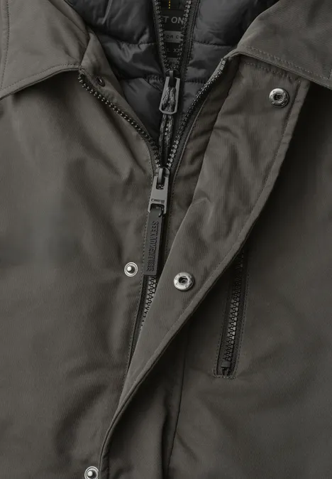 Nahaufnahme einer dunkelgrünen Jacke mit Reißverschluss, Druckknöpfen und wattierter Innenlage.