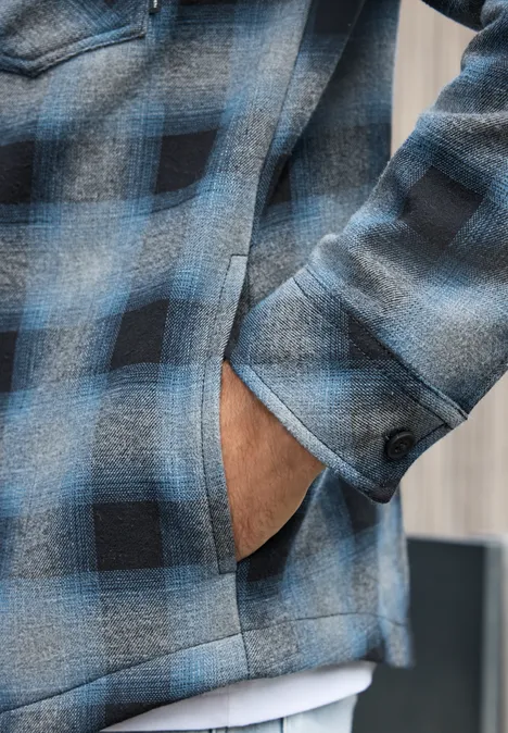 Gros plan sur une veste à carreaux bleu et noir, main dans la poche