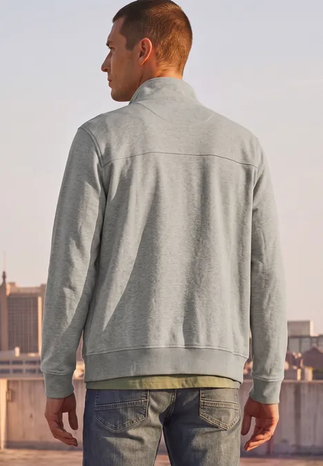 Ein Mann in grauer Jacke steht auf einem Dach und blickt auf die Stadt.