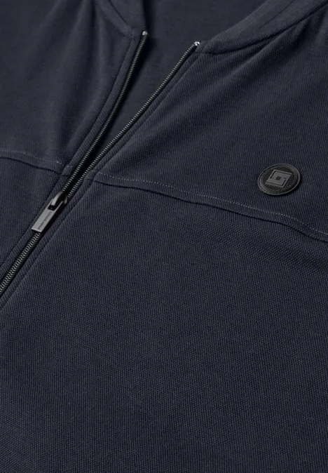 Nahansicht eines dunkelblauen Reißverschluss-Sweatshirts mit rundem Logo auf der Brust.