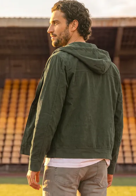 Ein Mann mit Kapuzenjacke steht auf einem Sportplatz neben leeren Tribünen.