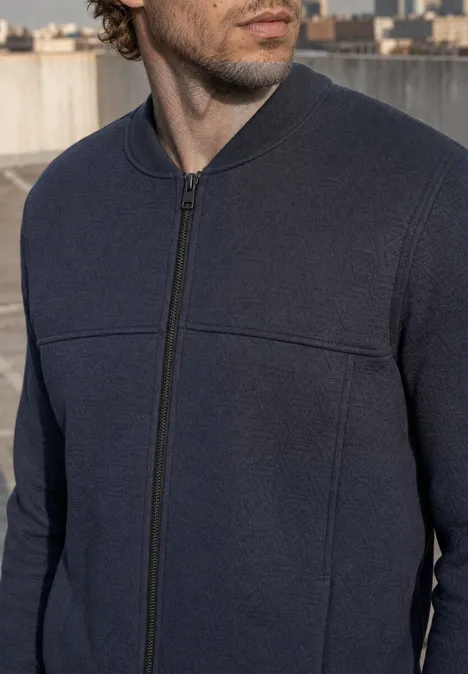 Blouson à structure 3D et fermeture zip dark ink blue Ein Mann in dunkelblauem Reißverschluss-Pullover auf einem Dach mit Stadt im Hintergrund.